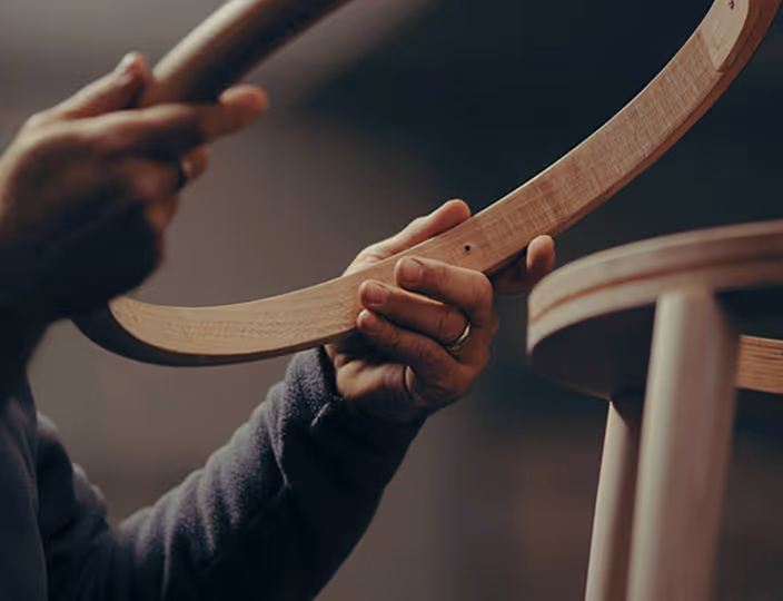 Close-up of hands holding and assembling a curved wooden chair part