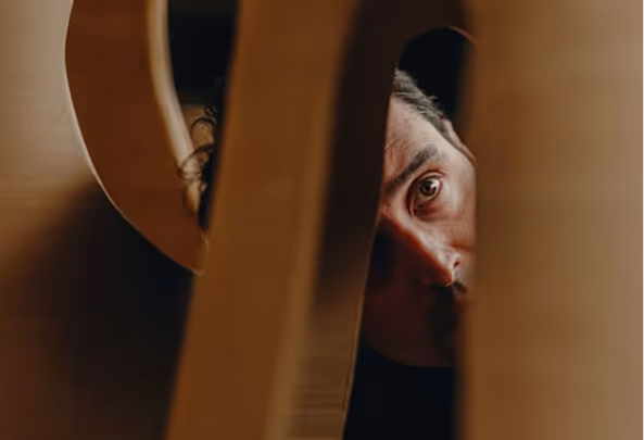 Close-up of a person's face partially visible through narrow wooden slats in warm lighting