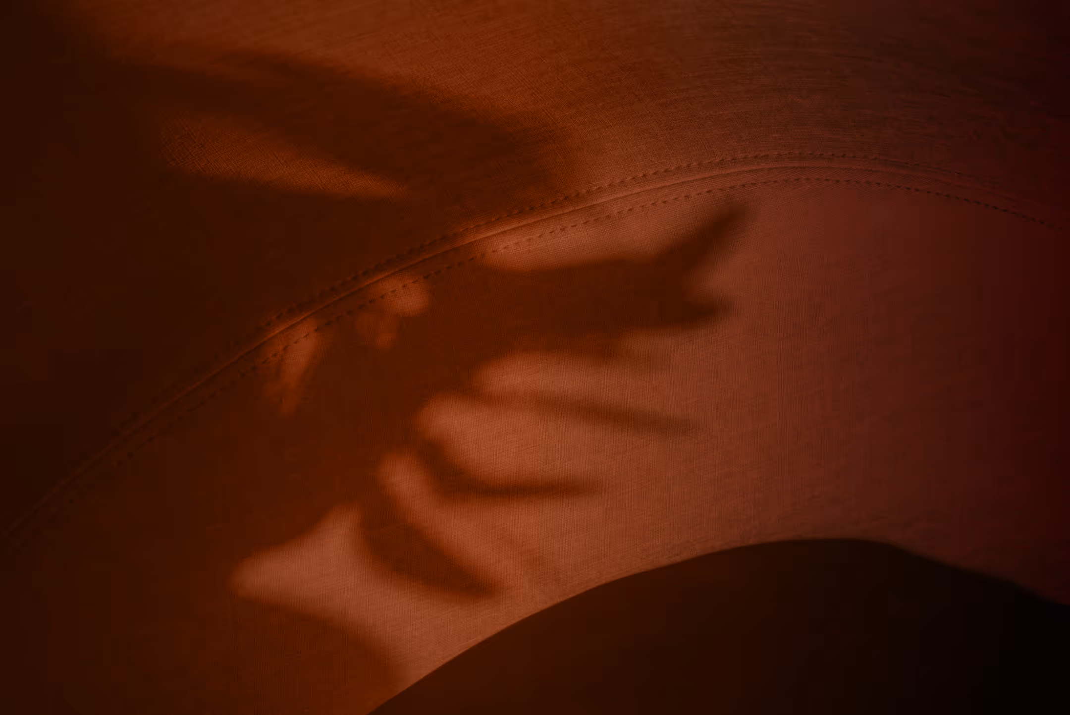 Shadow of a hand on textured fabric with stitching detail.